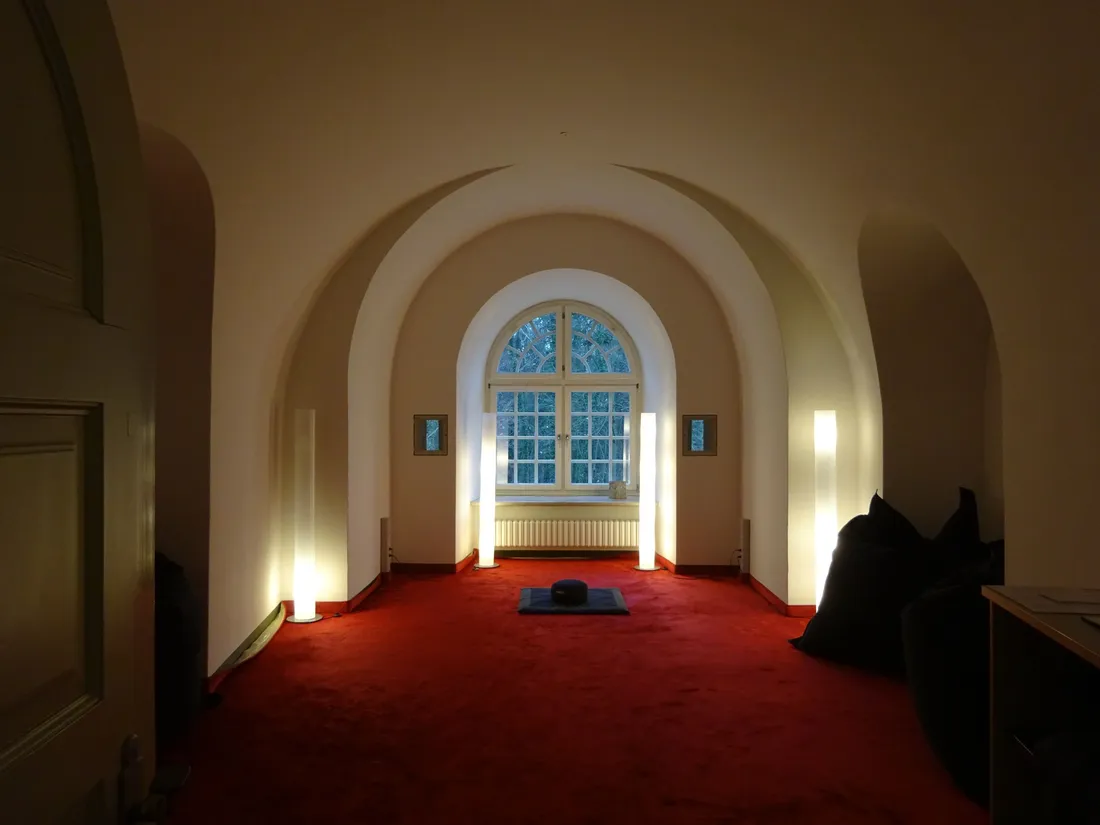 Ein dezent beleuchteter Raum mit rotem Teppichboden und hohem Rundbogenfenster
