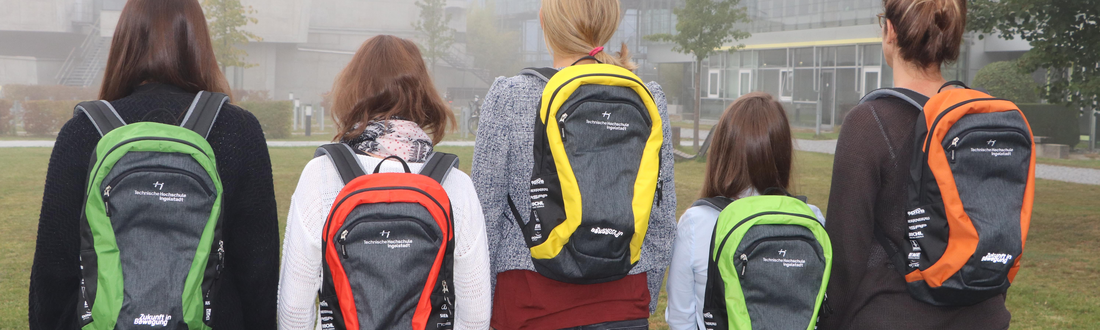Fünf Studenten mit THI-Rucksäcken in verschiedenen Farben auf dem Rücken auf dem THI-Campus