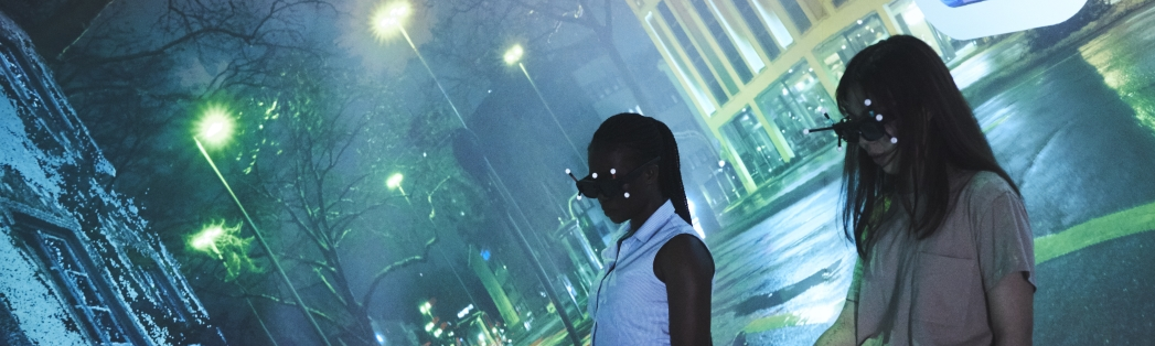Zwei Frauen in der CAVE im VR-Lab, Hintergrund bunte Straßenszene bei Nacht