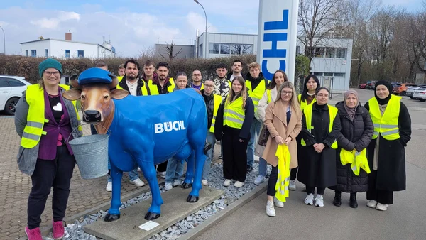 Group photo on the Büchl company premises, in the foreground a statue of a blue-colored cow, the participants wear yellow safety vests