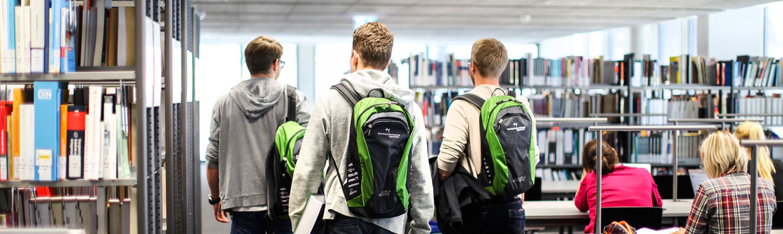 3 students with THI-rucksack walk through the library
