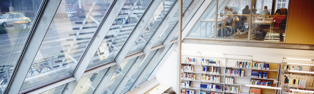 Blick in die Bibliothek mit Glasfront, Arbeitsplätzen und Bücherregalen