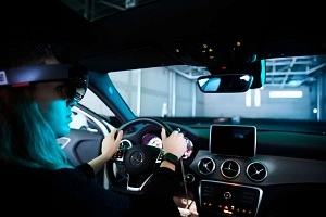 A student wearing virtual reality glasses sits in a test car a 