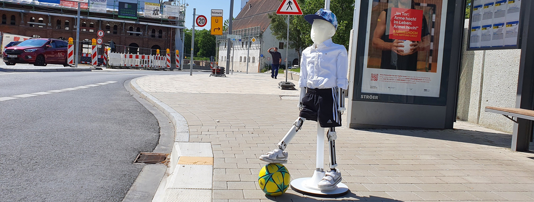 Abbildung des Kinderdummy mit einem Ball am Fuß an einer Straße
