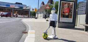 Abgebildet ist ein Kinder-Dummy mit einem Fußball an einer Bushaltestelle