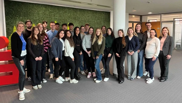 A large group of people are standing in the offices of the Sparkasse, with the large Sparkasse logo on the side. 