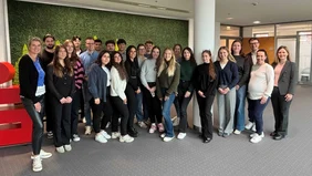 A large group of people are standing in the offices of the Sparkasse, with the large Sparkasse logo on the side. 