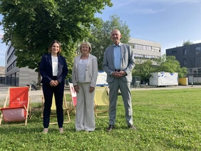 Portrait des Hochschulpräsidenten sowie der Vizepräsidentinnen auf einer Wiese, im Hintergrund die Hochschule