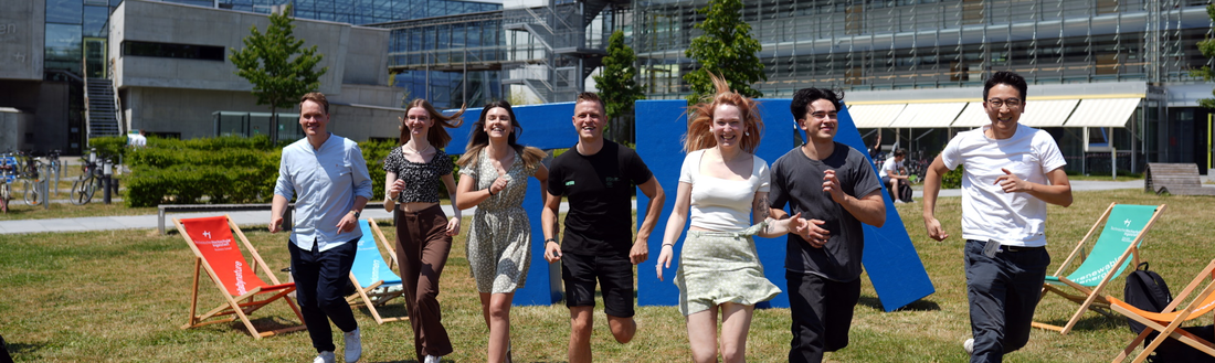 Studierende laufen auf der Campuswiese in einer Reihe Richtung Kamera