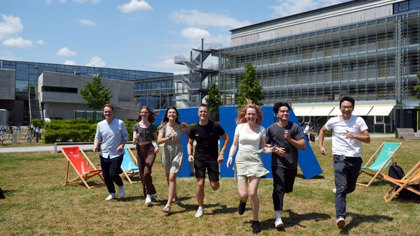 Studierende laufen auf der Campuswiese in einer Reihe Richtung Kamera