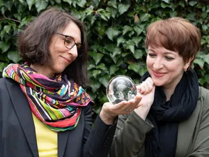 Zwei Frauen Blicken auf eine Glaskugel, die eine von beiden in der Hand hält