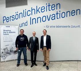 Bild von drei Männern in der Aula der THI mit einem Banner von VDE Bayern im Hintergrund