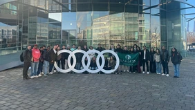 A group photo in front of the Audi Museum, the Babson College flag is shown in the centre of the group