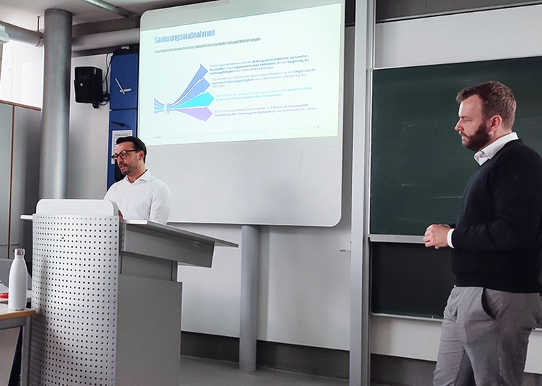 Two men standing in front of a whiteboard displaying a presentation.