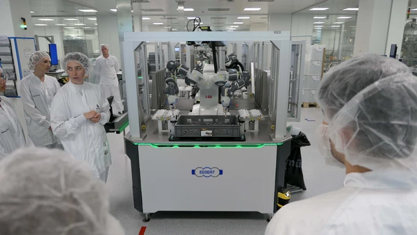 You see people in sterile suits watching a robot with several arms.