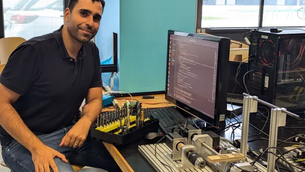 mann an einem Schreibtisch, der mit einem Set aus verschiedenen Bohrern vor einem Bildschirm sitzt, neben ihm eine Bohrvorrichtung