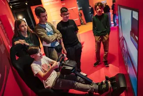 Junge Besucher des MS-Wisschenschaft Science Center, die an und um eine Fahrsimulation sitzen