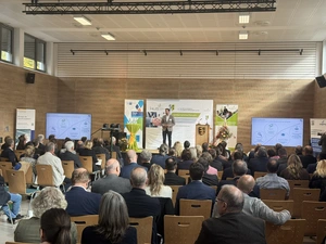 Eine männliche Person auf einer Bühne stehend hält einen Vortrag vor einem großen Publikum