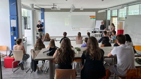 In the lecture hall: from the back you can see students listening to a man at the front of the white board.