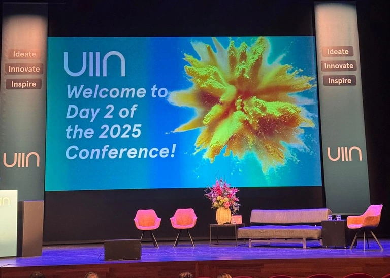 Foto der Bühne mit der Präsentation im Hintergrund auf der steht: UIIN Welcome to Day 2 of the 2025 Conference!