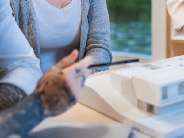 ein Mann und zwei Frauen begutachten Architekturmodell eines Gebäudes