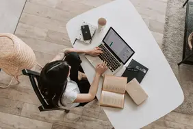 Eine Studentin sitzt mit Laptop und Büchern an einen Tisch
