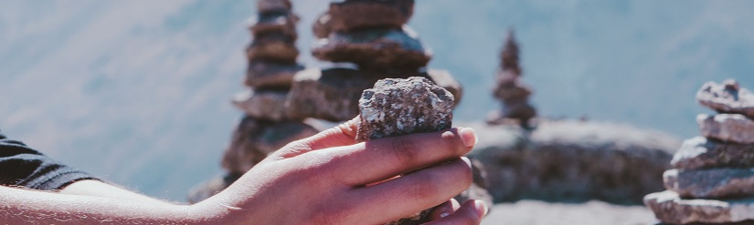 One hand holds a small tower of stones, in the background more stone towers