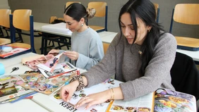 Two female people stick paper cut-outs on a sheet
