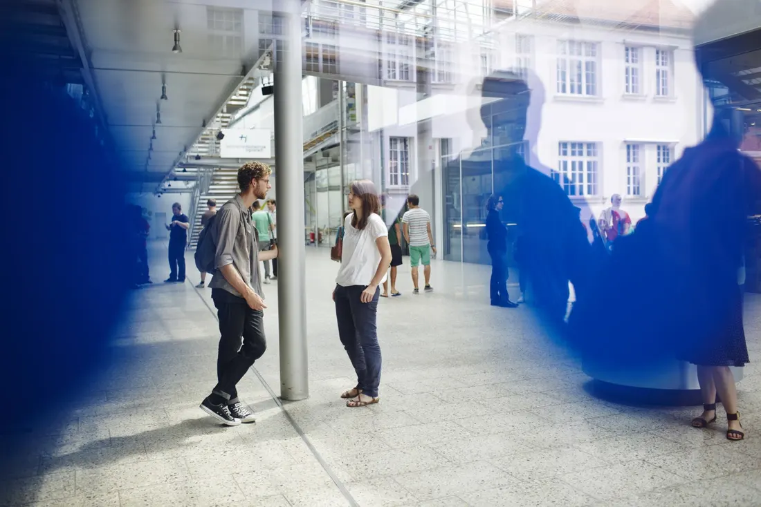 Zwei Studierende unterhalten sich, im Hintergrund Gebäude B