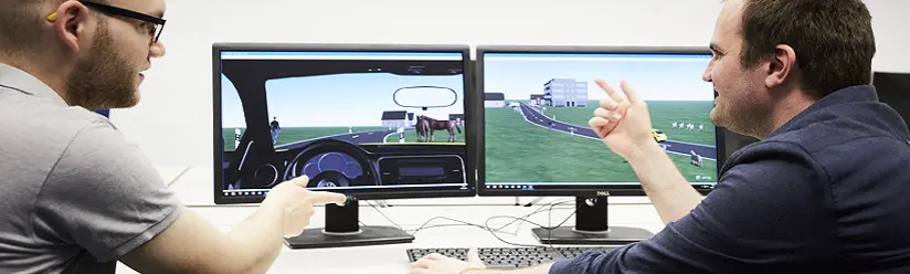 Two research assistants discuss a driving simulation on the screen