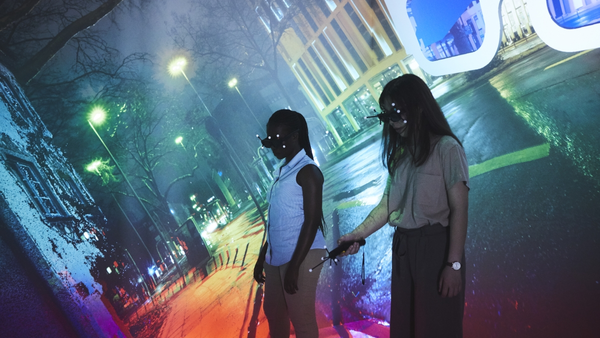 Zwei Frauen in der CAVE im VR-Lab, Hintergrund bunte Straßenszene bei Nacht