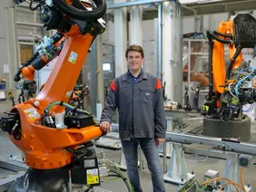 Professor Tröber stehend neben einem Fertigungsroboter in den Hallen der Audi AG