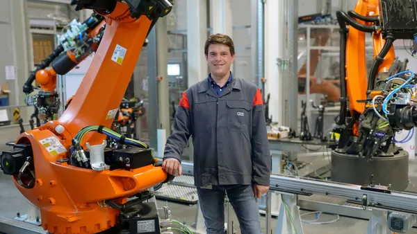 Professor Tröber stehend neben einem Fertigungsroboter in den Hallen der Audi AG