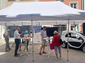 Abbildung des Forschungsfahrzeugs ANTON (Renault Twizy), sowie Bürgerinnen und Bürger im Austausch mit Prof. Vaculin
