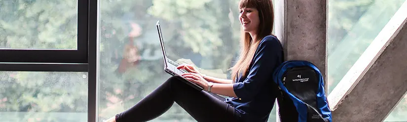 Eine Studentin sitzt in einem Fensterrahmen und arbeitet am Laptop