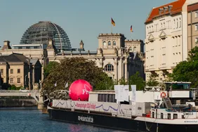 Bild mit Blick auf das schwimmende Science Center der MS-Wissenschaft auf der Spree, im Hintergrund das Reichstagsgebäude 