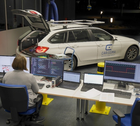 Image of a woman sitting in front of two screens. On which system tests of applications based on Car2X communication are running