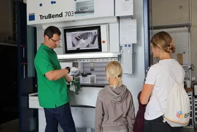 Mann zeigt Kind und Frau Ergebnis aus der Werkzeugmaschine