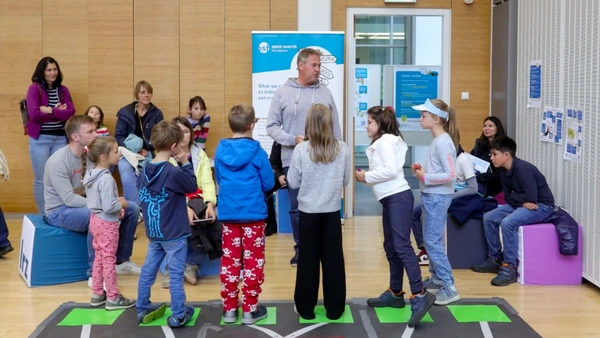 : A man speaking to a group of children, their parents monitoring the game.