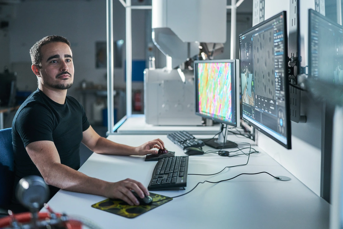 Eine männliche Person sitzt am Schreibtisch und blickt auf einen Bildschirm