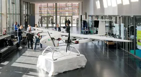 Einblick in das Urban Air Mobility Treffen in der Aula der THI, zusehen sind Ausstellungsmodelle sowie Gastgeber und Teilnehmer