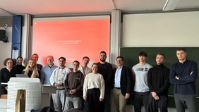 A group photo in a lecture hall, with the presentation and a blackboard in the background. 