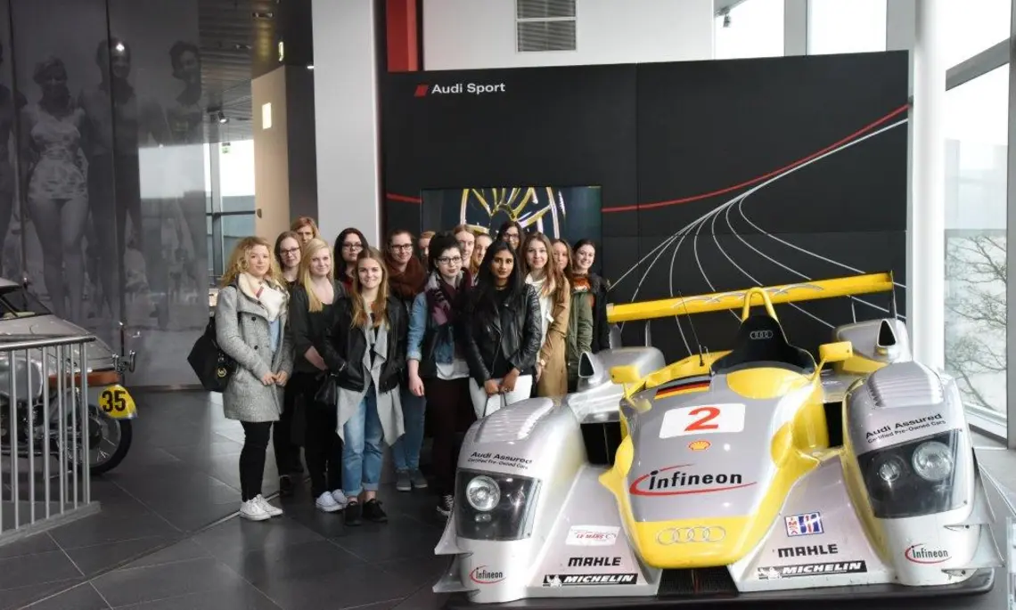 Eine Gruppe Studentinnen stehen neben einem Audi-Rennwagen im museum mobile