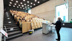 Eine Frau referiert vor einem vollen Hörsaal. 