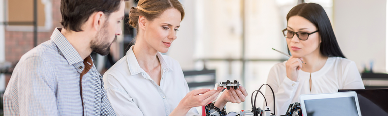 Drei Personen betrachten technische Bauteile 