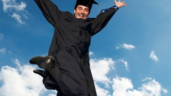 A jubilant doctoral candidate with a doctoral hat jumps into the air