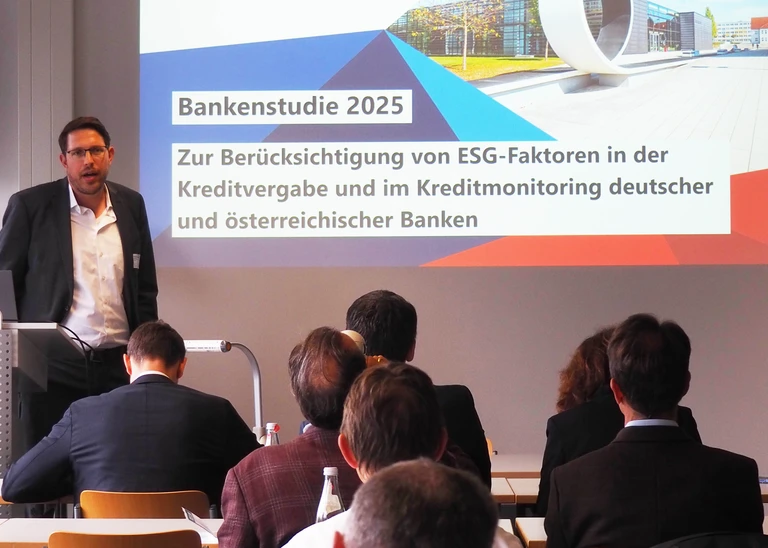 A person is giving a presentation; behind them, on the wall, you can see a slide from a PowerPoint presentation.
