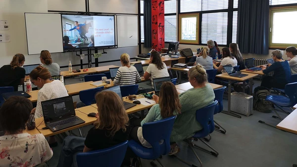 Ein Hörsaal von hinten, man sieht eine große Anzahl Erwachsener mit Laptops vor sich.