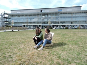 Zwei Studentinnen sitzen auf dem Solarschaukelstuhl auf der Campuswiese