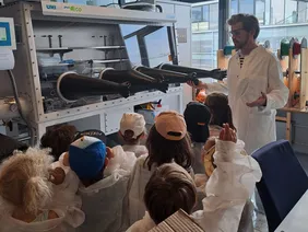 Philipp Lang begrüßt die Kleinen an der THI (Foto: THI). Philipp Lang präsentiert den KiGa-Kindern etwas, alle mit Schutzkleidung